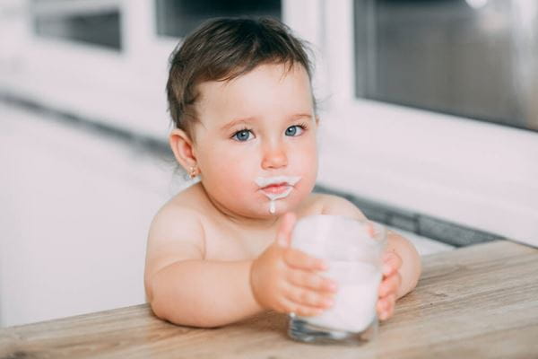 A little girl in the kitchen drinking milk