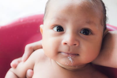 A baby has spit up some milk on their chin