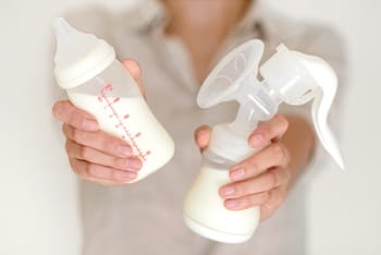 Breast pump and bottle with milk in a woman's hands with a blurred background