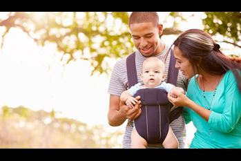 Family With Baby Son In Carrier Walking Through Park