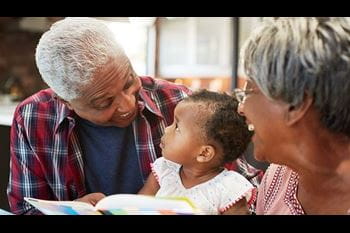Grandparents Reading Book With Baby Granddaughter At Home