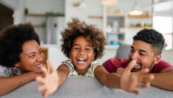 Happy child reaching towards the camera with his parents on each side of him.