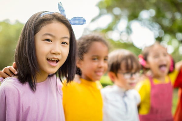 group of children standing close together outdoors with arms around each other wearing colorful shir