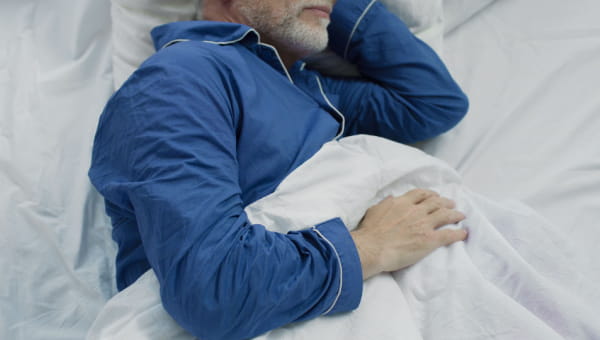 Health Sleep, Healthy Aging A senior male laying in bed comfortably asleep in blue pajamas.