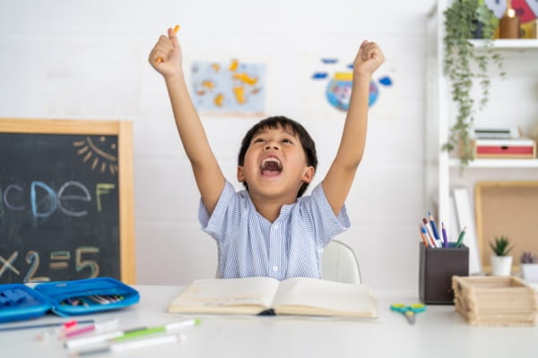 A school boy raising his hands cheering in a classroom.