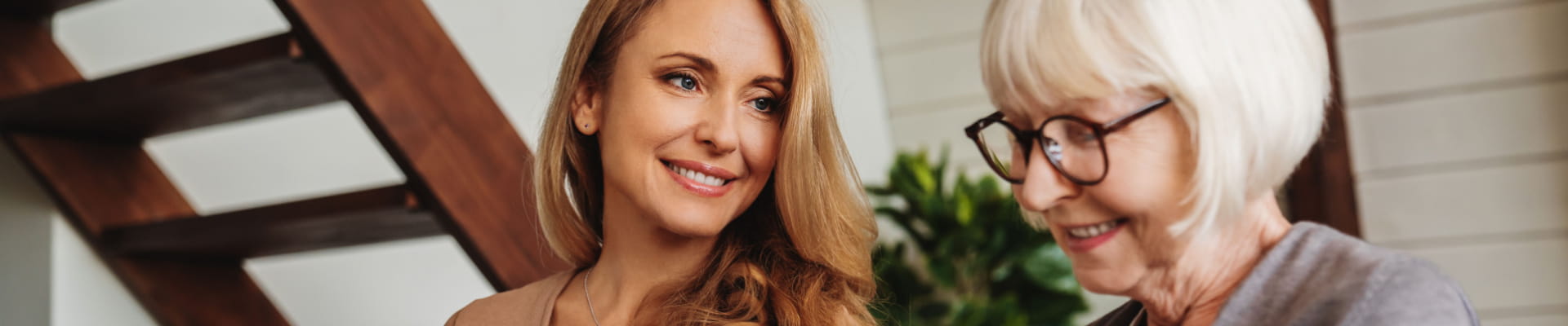 A young woman smiling at an older woman sitting together inside.